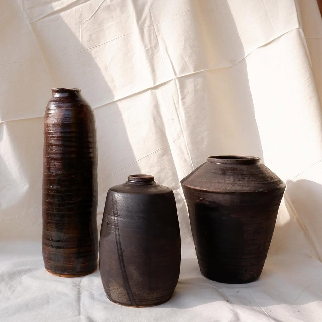 Three dark, earthy Studio Sira ceramic vessels in sunlight